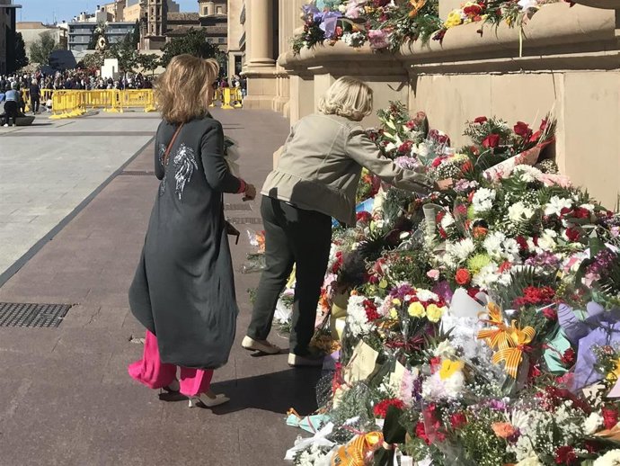 Dos mujeres colocan flores a la virgen del Pilar en la fachada de la basílica
