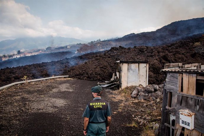 20 September 2021, Spain, El Paso: Smoke rises in front of a Guardia Civil official from cooling lava that has flowed over a road on the Canary island of La Palma.