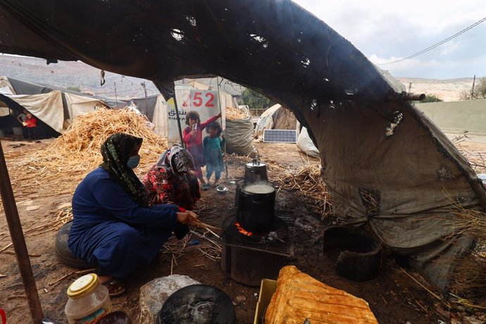 12 October 2021, Syria, Idlib: A woman prepares food for her children in a tent at the Armanaz camp, northwest Syria. The displaced towards northwest Syria and those residing in random camps are preparing for the winter, in conjunction with the high pri
