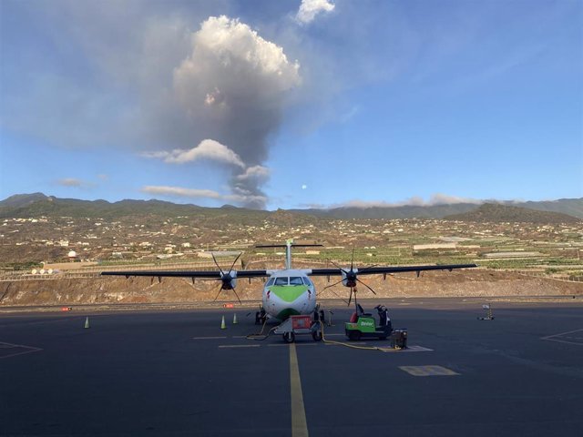 A Binter plane on the La Palma airport runway, with the erupting volcano in the background