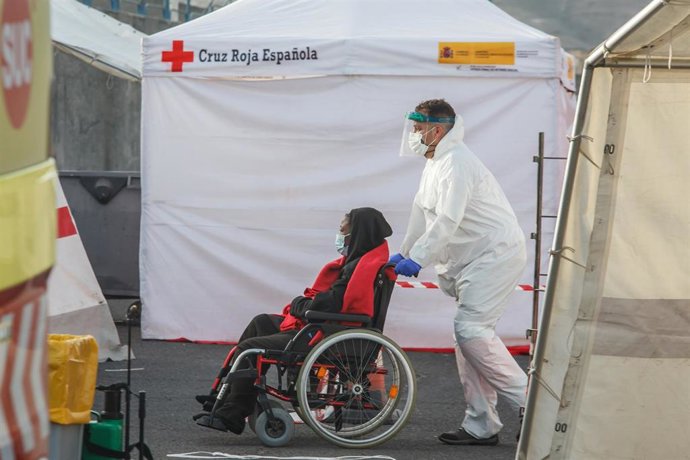 Archivo - Un trabajador lleva en silla de ruedas a una mujer rescatada por Salvamento cuando iba a bordo de una patera