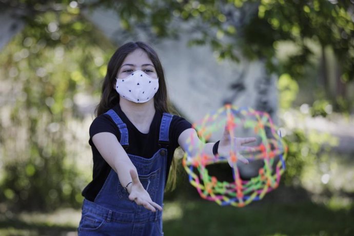 Archivo - Niña de 11 años jugando con una bola expandible con una mascarilla de protección en un espacio al aire libre