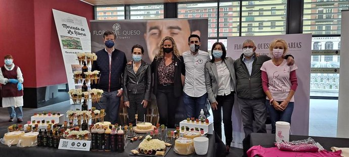 Yolanda Díez y Santiago Mohedano, junto a miembros de Acambi reparten flores de queso solidarias contra el cáncer de mama en el Mercado de La Ribera de Bilbao.