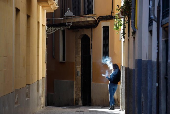 Archivo - Una mujer fuma en una calle vacía en Palma.
