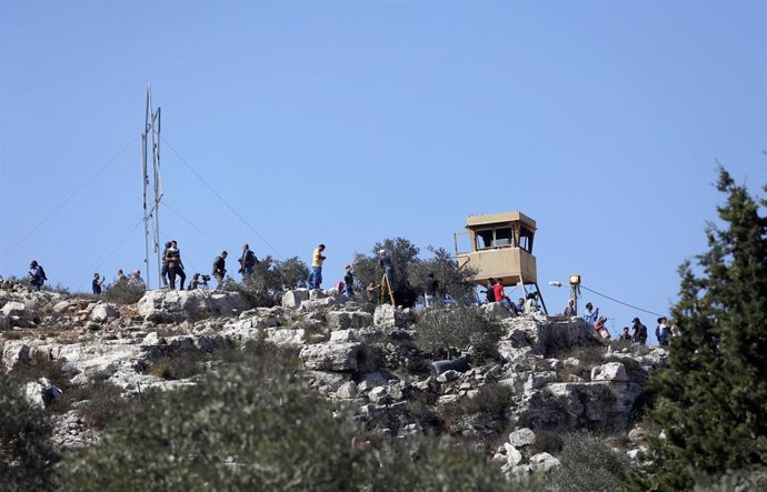 Palestins recullen olives enfront d'un lloc avanat israeli en Nablus