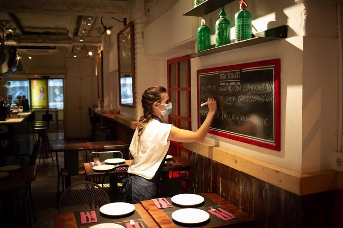 Una camarera apunta platos en una pizarra en el interior de un bar 