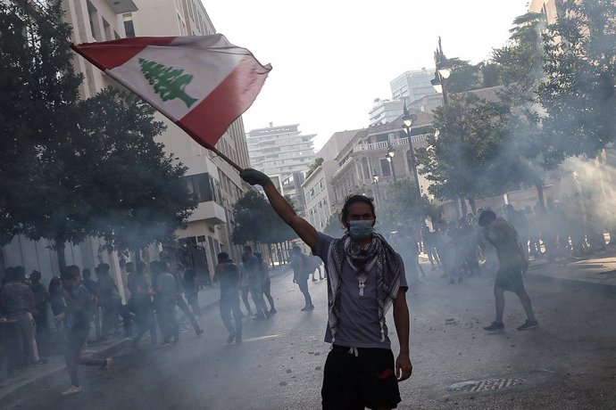 Archivo - 10 August 2020, Lebanon, Beirut: An anti-government activist flies the Lebanese national flag during clashes with riot police in Beirut's downtown. The Lebanese government resigned following the massive Beirut port explosion of 04 August which