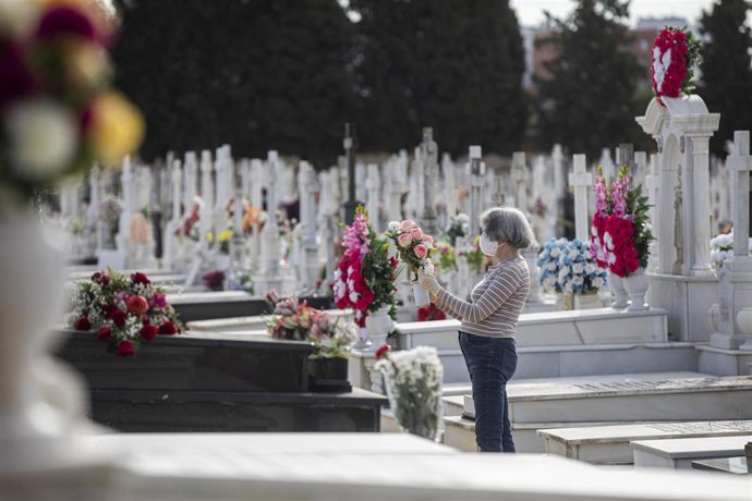 Archivo - Una mujer coloca flores en una de las lápidas de un cementerio