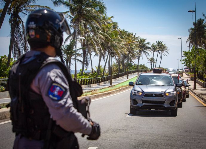 Archivo - 22 April 2020, Puerto Rico, San Juan: A police officer blocks the way in front demonstrators protesting in their cars to demand more Coronavirus (Covid-19) tests to be carried out among the population and a plan for a rapid economic recovery f