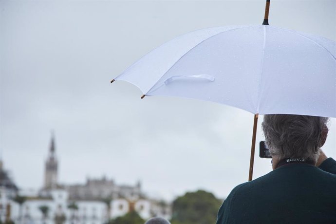 Un señor, bajo su paraguas, toma una foto con su móvil del río Guadalquivir en un día lluvioso del puente de Todos los Santos el 30 de octubre de 2021 en Sevilla (Andalucía, España)