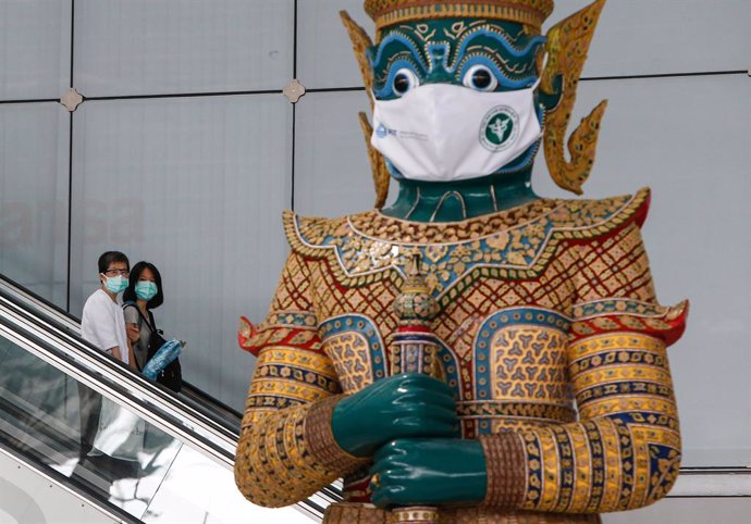 Archivo - 28 April 2021, Thailand, Bangkok: People wearing face masks pass a giant statue wearing a face mask at Suvarnabhumi Airport. Health  Ministry and the Airport Operation Centre set up a new vaccination centre for aviation-related personnel. Phot
