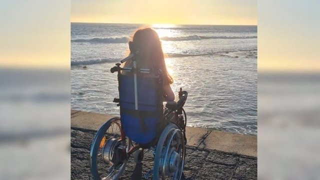 Una joven en silla de ruedas mirando al mar.