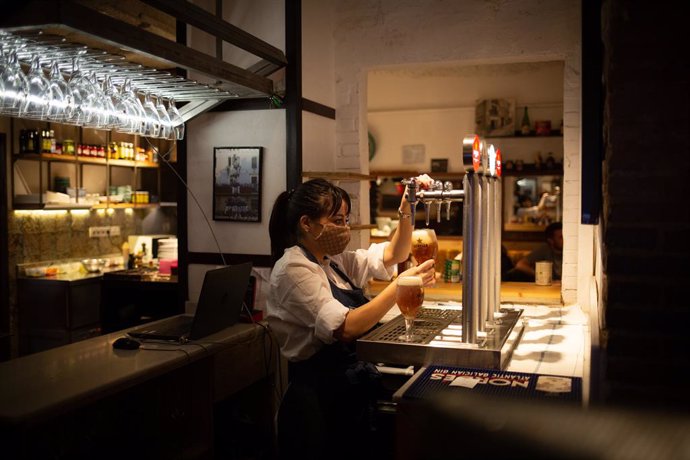 Una camarera sirve una cerveza en el interior de un bar en una calle céntrica de Barcelona, a 14 de octubre de 2021, en Barcelona, Catalunya (España). A partir de este viernes en Cataluña se terminarán las limitaciones de aforo en los equipamientos cult
