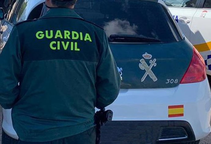 Archivo - Un agente de la Guardia Civil de espaldas y junto a un vehículo oficial del cuerpo