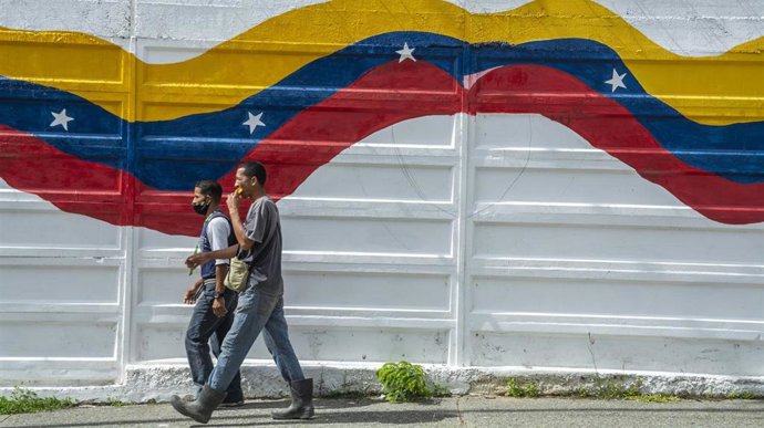 Archivo - Dos personas pasan ante un mural con la bandera de Venezuela en Caracas