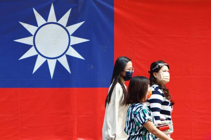 October 28, 2021, Taipei, Taiwan: People wearing masks walk past a Taiwan flag, amid rising tensions between Taipei and Beijing and military threats from China. The self governing island has been facing intensifying threats from China whilst building be