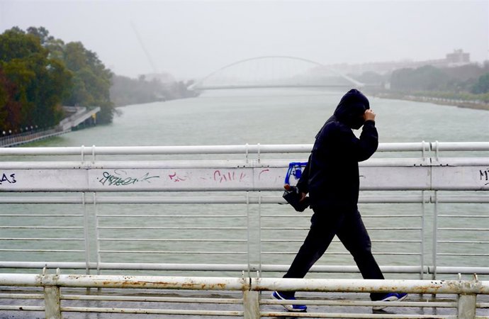 Archivo - Imagen de archivo de un persona protegiéndose de la lluvia y el viento en Sevilla