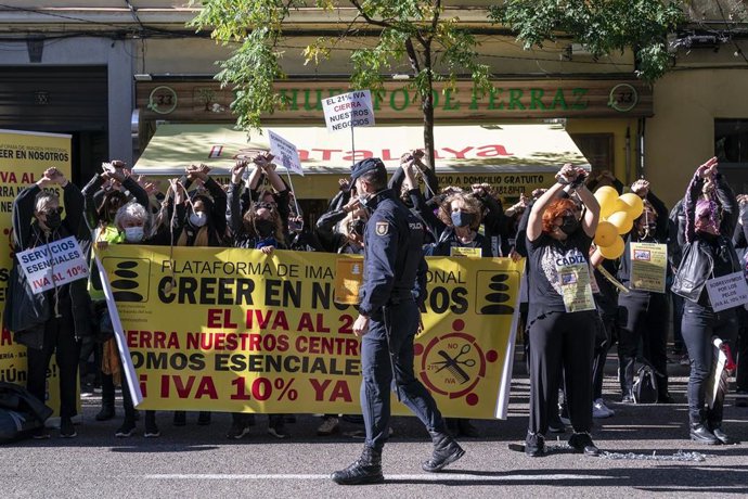 Un agente de policía supervisa a un grupo de personas perteneciente al sector de la estética durante una concentración por la bajada del IVA a la imagen personal ante la sede del PSOE 