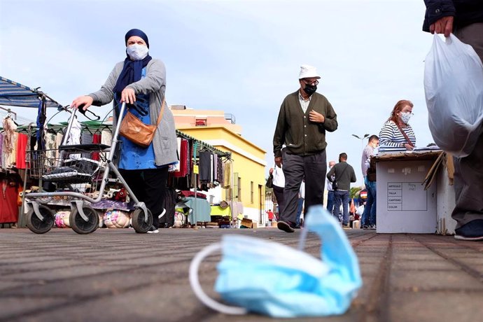 Archivo - Una mascarilla quirúrgica en el suelo mientras varias personas caminan por el rastro de Melilla