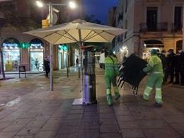 Trabajadores municipales retiran mesas de una terraza.
