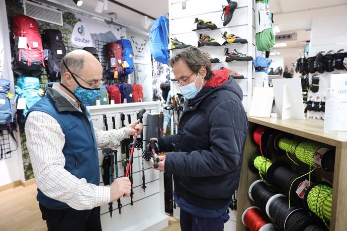 Archivo - Un trabajador de una tienda en la venden y alquilan material para la nieve muestra varios bastones de esquí a un cliente