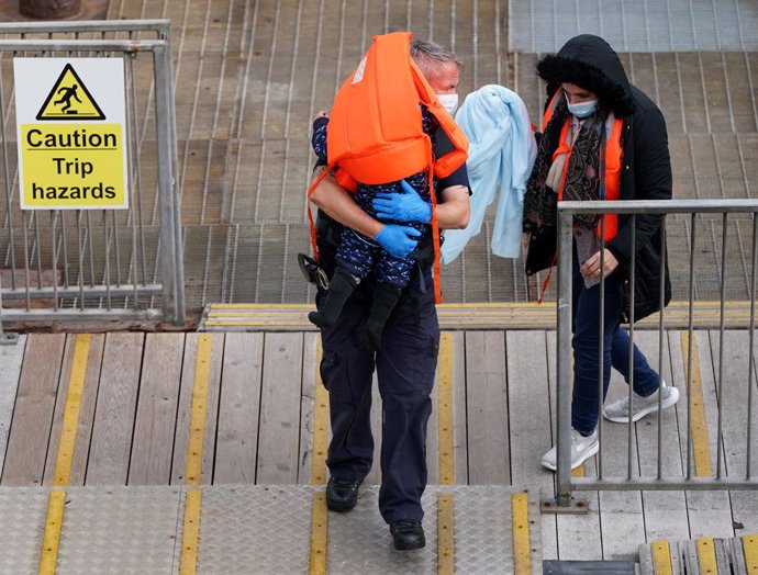 Archivo - 26 September 2021, United Kingdom, Dover: A British border force officer escorts a woman and a child as a group of people thought to be migrants are brought into Dover, by a Border Force patrol boat, following a small boat incident in the Engl