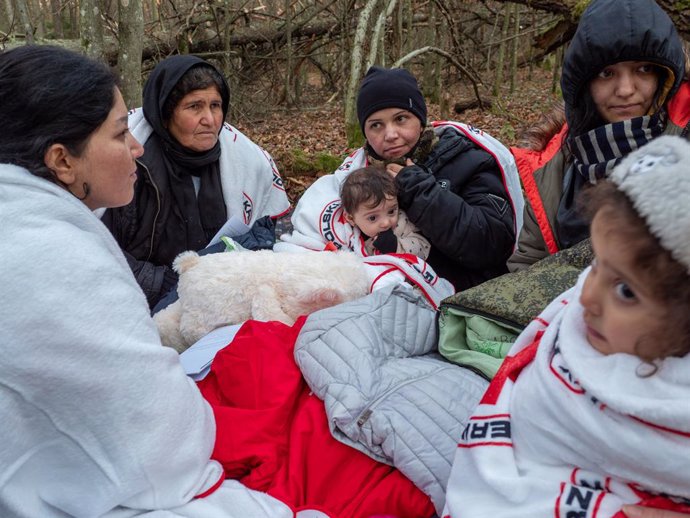 FILED - 09 November 2021, Poland, Narewka: Arefugee family warms themselves under blankets provided by Grupa Granica organization, as they sit in a forest near the Belarusian-Polish border. The Iraqi refugee family of seventeen, including nine children