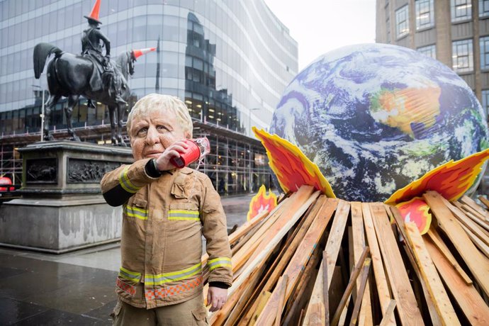 12 November 2021, United Kingdom, Glasgow: An activist dressed as Britain's Prime Minister Boris Johnson pours water in front of a model repreenting the globe on a pyre during an Oxfam protest on conjunction with the United Nations Climate Change Confer
