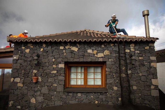 Varios voluntarios trabajan retirando cenizas de los tejados de varias casas próximas al volcán de Cumbre Vieja