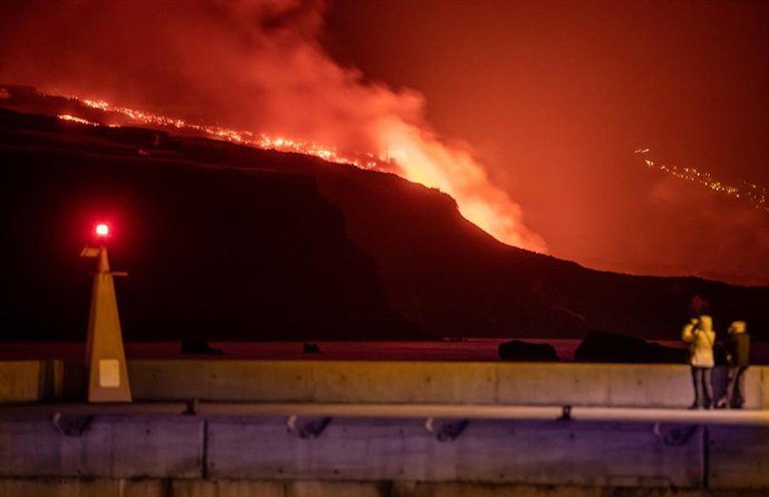 Varias personas observan la lava y piroclastos a su llegada a la playa de los Guirres