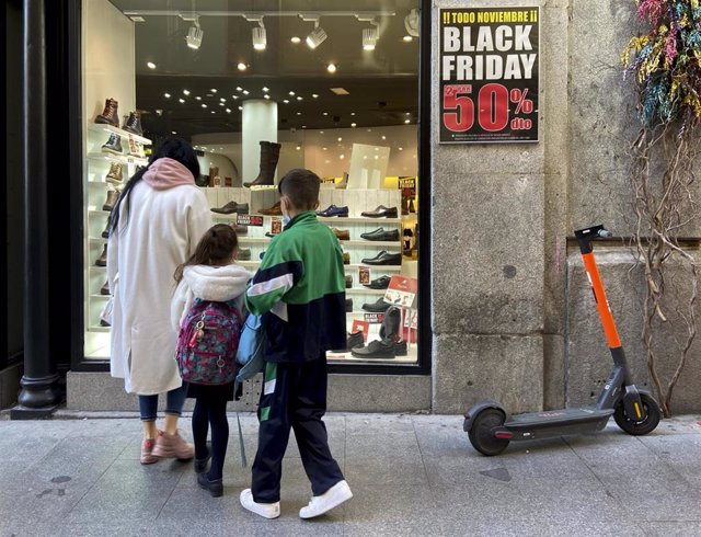 Varias personas en el escaparate de un comercio que anuncia descuentos del 50% por el Black Friday