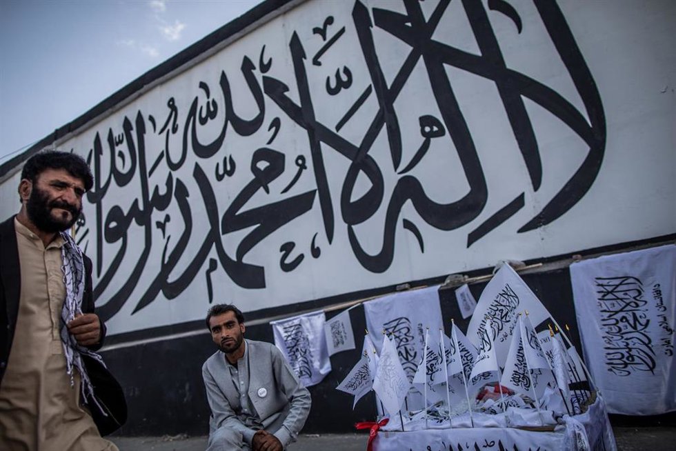 Archivo -  Un hombre afgano vende banderas talibanes con el credo musulmán escrito en una pared de la antigua embajada de Estados Unidos en Kabul.