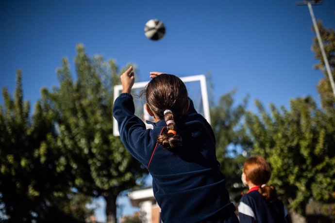 Una niña juega al baloncesto en el patio de un colegio.