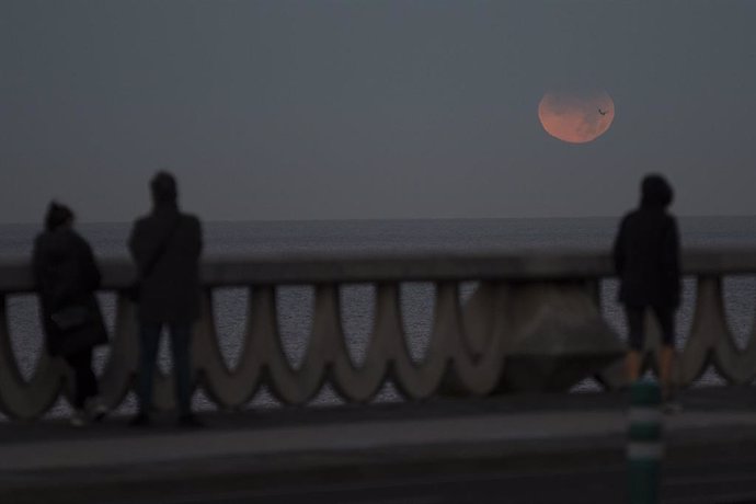 Tres personas observan el eclipse lunar parcial desde A Coruña, a 19 de noviembre de 2021, en A Coruña, Galicia, (España).