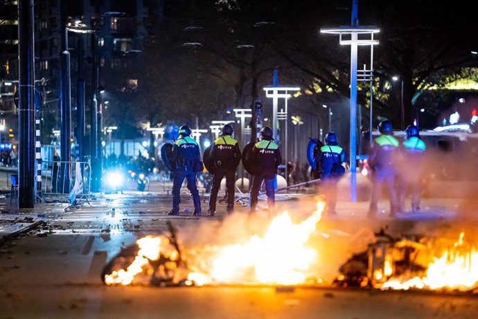 19 November 2021, Netherlands, Rotterdam: Police officers stand in front of a fire during a protest against the 2G policy at the Coolsingel. Violent riots broke out in the Dutch port city of Rotterdam during a demonstration by hundreds of people against