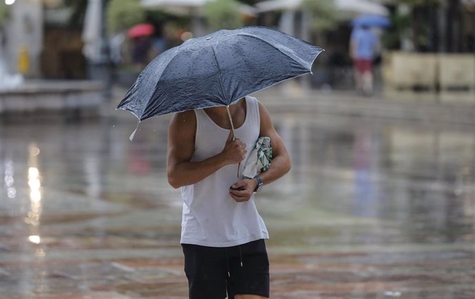 Archivo - Una persona sostiene un paraguas mientras llueve.