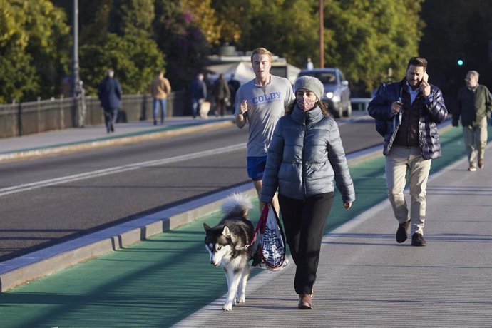 Una señora, abrigada, pasea a su perro durante el primer día de frío, a 23 de noviembre de 2021 en Puente de Triana en Sevilla (Andalucía, España)