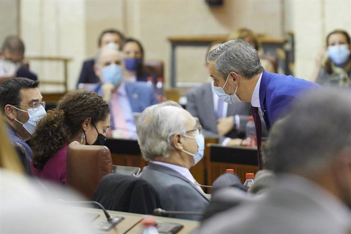 El consejero de Hacienda y Financiación Europea, Juan Bravo, (d) se acerca al escaño de la portavoz de l grupo parlamentario Unidas Podemos, Inmaculada Nieto, (i) durante el Debate de Presupuesto de la Junta de Andalucía, a 24 de noviembre de 2021 en el