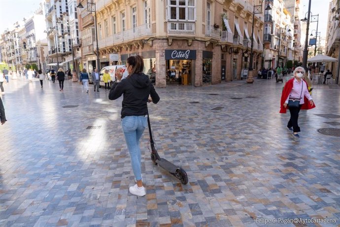 Una mujer camina portando un patinete