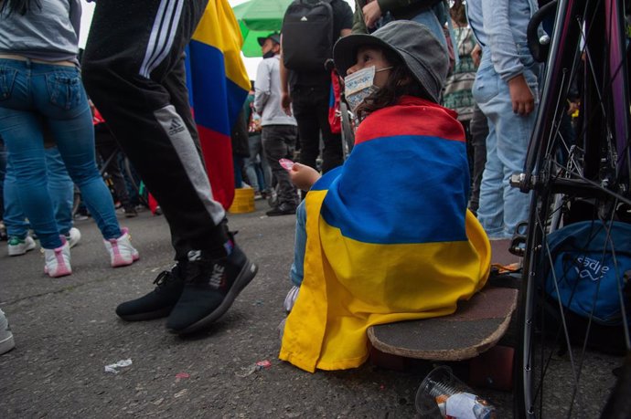 Archivo - Una niña se sienta en una patineta con una bandera de Colombia envuelta en su espalda en una jornada de protestas en Bogotá.