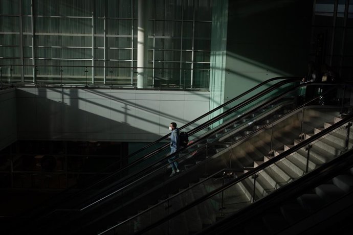 Un home amb una maleta en les escales mecniques de l'Aeroport del Prat, a Barcelona