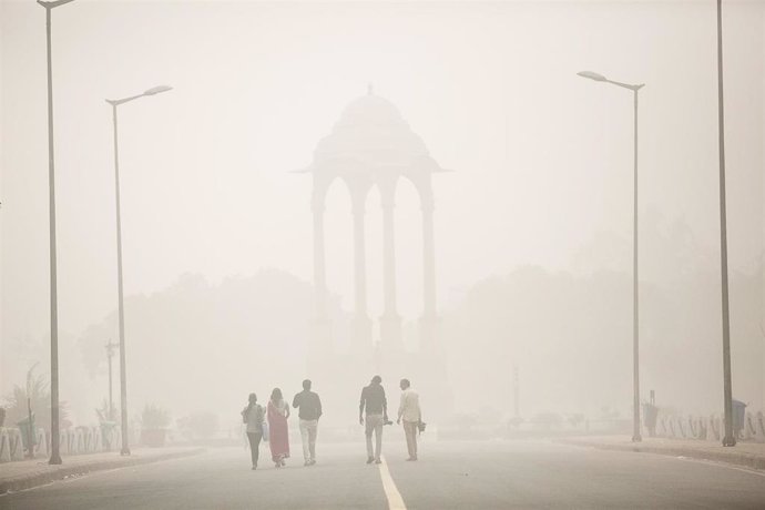 Archivo - Un grupo de personas camina por las calles de Nueva Delhi entre una nube de contaminación.