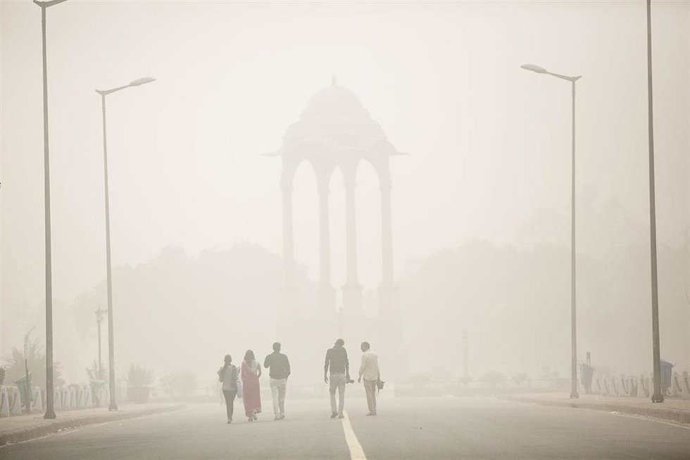 Archivo - Un grupo de personas camina por las calles de Nueva Delhi entre una nube de contaminación.