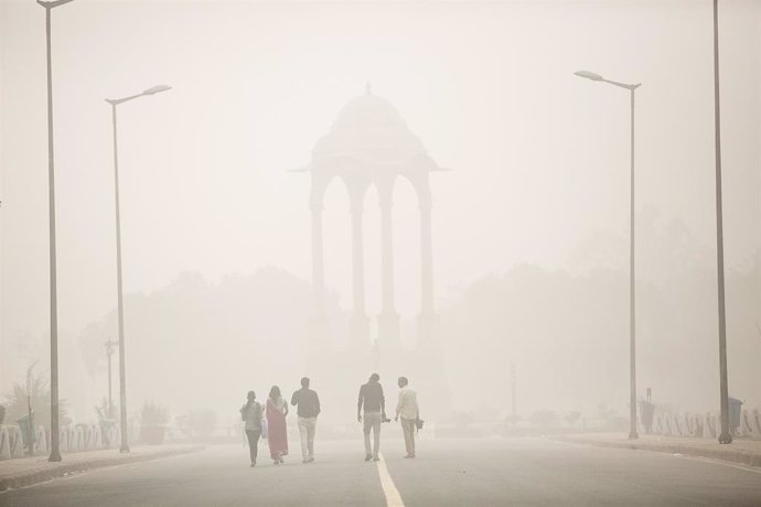Archivo - Un grupo de personas camina por las calles de Nueva Delhi entre una nube de contaminación.