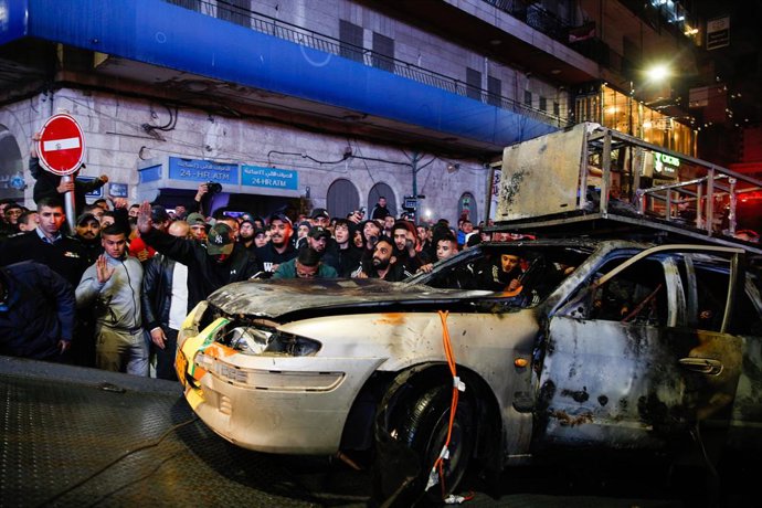 01 December 2021, Palestinian Territories, Ramallah: Locals gather around the remains of a burnt Israeli car being transported away by Palestinian security forces, after the vehicle was set on fire by Palestinian youths upon it entering Ramallah. Photo: