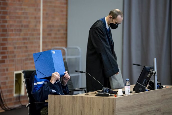 02 December 2021, Brandenburg, Brandenburg/Havel: The defendant, a 101-year-old former concentration camp guard, covers his face with a file as he attends a hearing at a courtroom, next to his lawyer Stefan Waterkamp (R). The man stands trial over accus