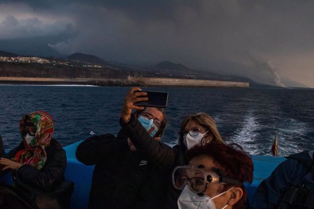 Un grupo de turistas fotografían la erupción volcánica en un barco que sale desde el puerto de Tazacorte