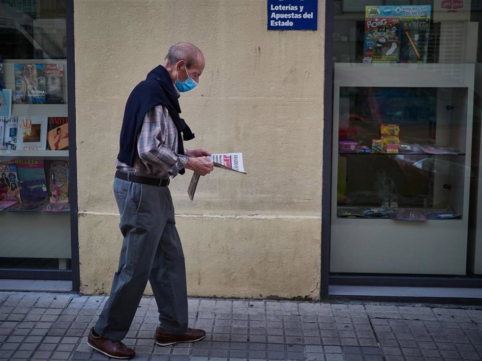 Archivo - Un hombre camina con mascarilla leyendo un periódico (archivo)