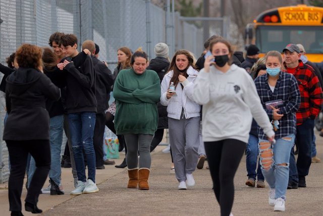 30 November 2021, US, Oxford: Parents walk away with their kids from the Meijer parking lot, where many students gathered following an active shooter situation at Oxford High School. Police took a suspected shooter into custody and there were multiple vic