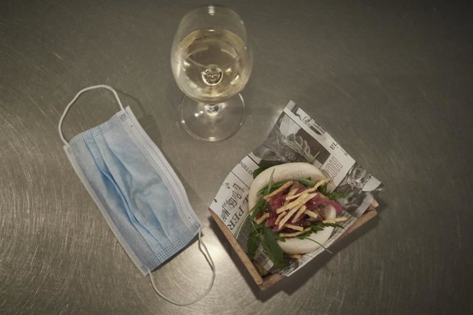 Archivo - Una copa de vino llena, junto a una mascarilla y una tapa.